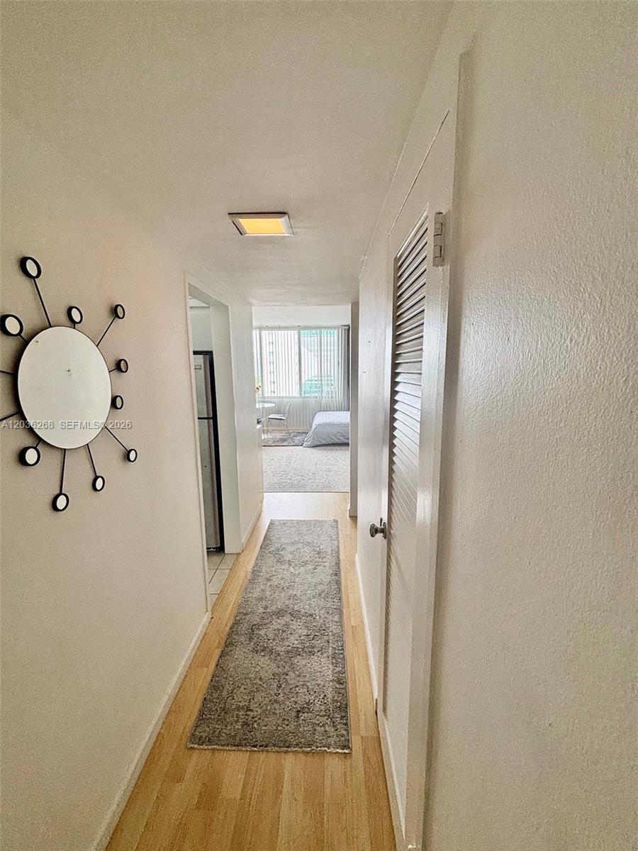 A hallway with light wood flooring leads past a louvered door to a bedroom — 1000 West Ave # 822, Miami Beach FL 33139, MIAMI BEACH, FL