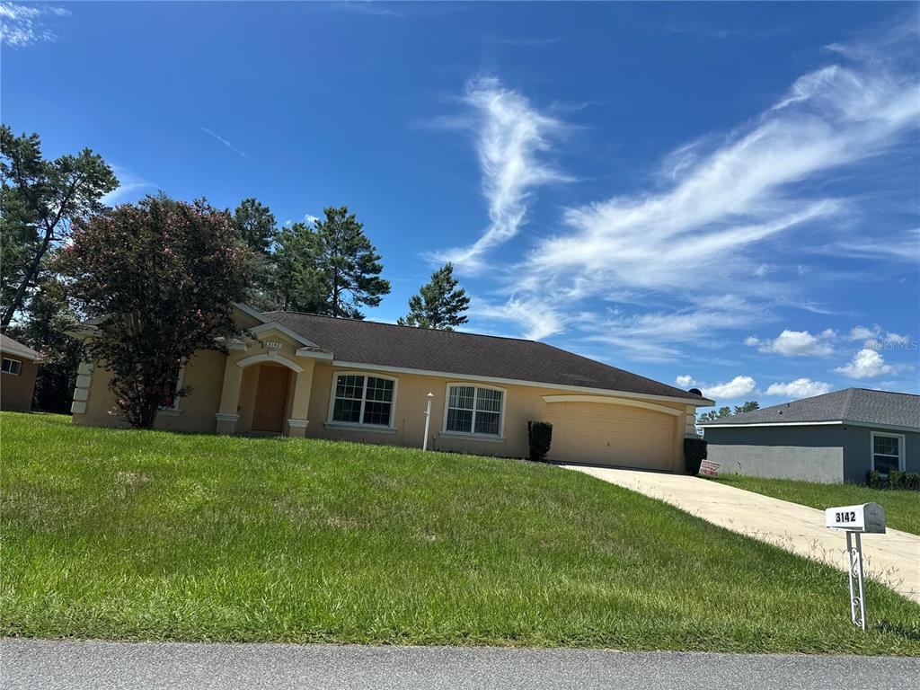 A single-story house with a tan stucco exterior, a two-car garage, and a grassy lawn — 3142 SW 132ND LANE, OCALA, FL