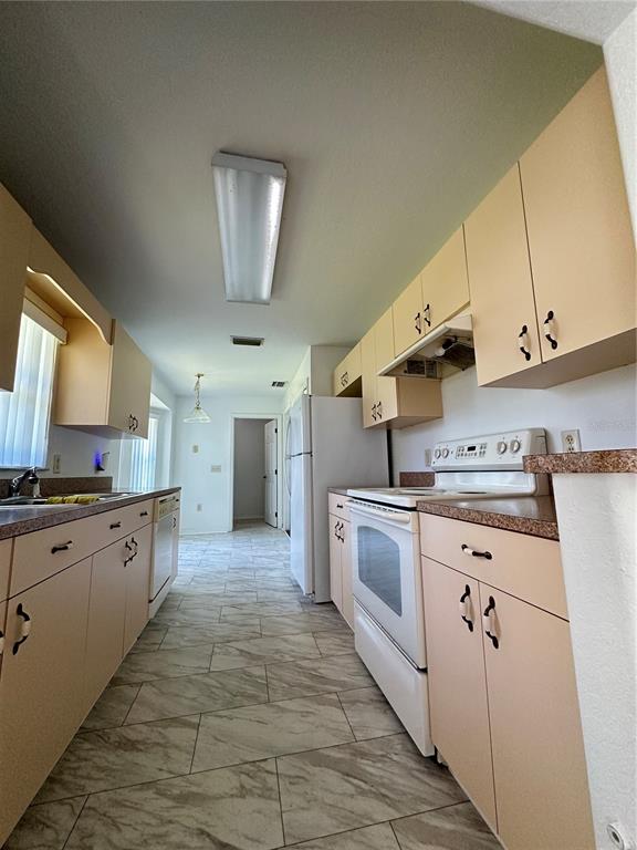 A kitchen features light-colored cabinets, white appliances, and gray tile flooring — 3142 SW 132ND LANE, OCALA, FL
