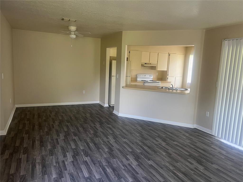 An open-concept living room features dark wood-look flooring and a pass-through window to the kitchen — 7266 POND CIRCLE, SPRING HILL, FL