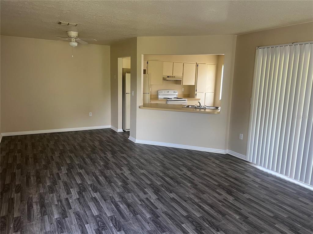 An open-concept living room features gray wood-look flooring and a pass-through window to the kitchen — 7266 POND CIRCLE, SPRING HILL, FL