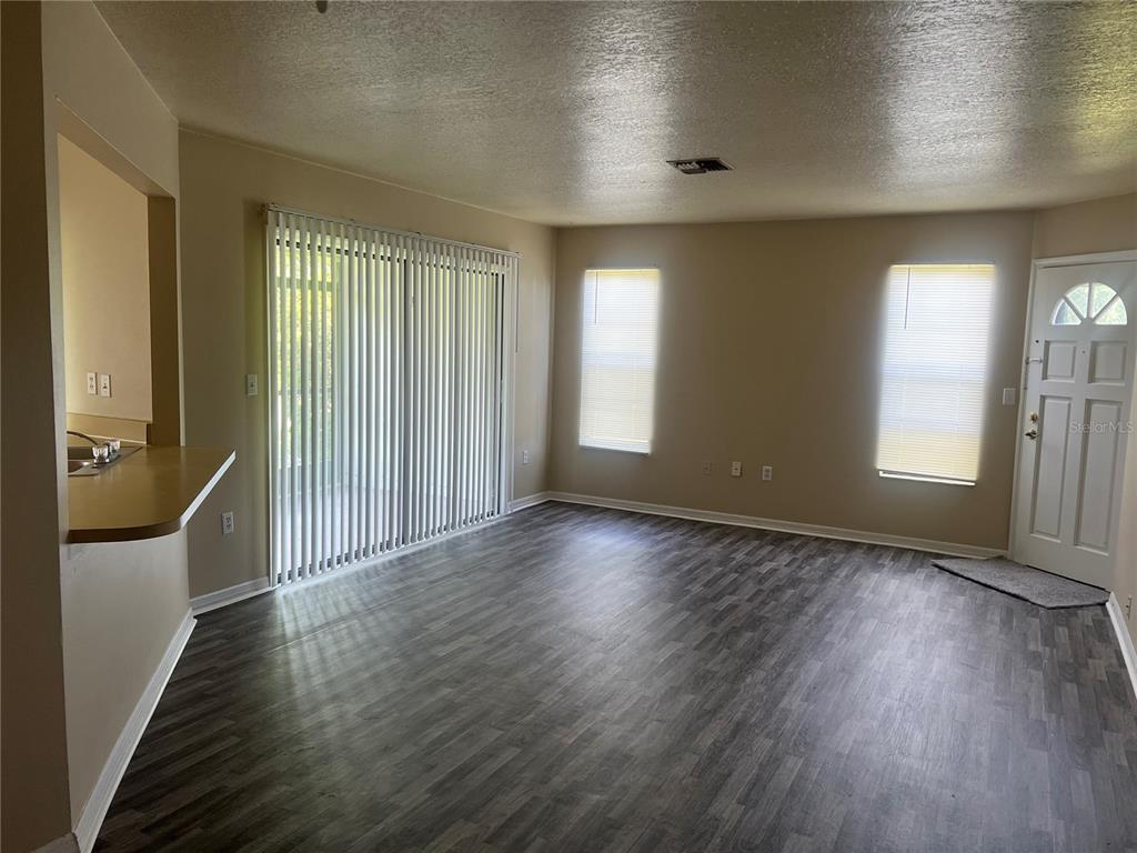 An open-concept living room features wood-look flooring, vertical blinds, and a kitchen breakfast bar — 7266 POND CIRCLE, SPRING HILL, FL