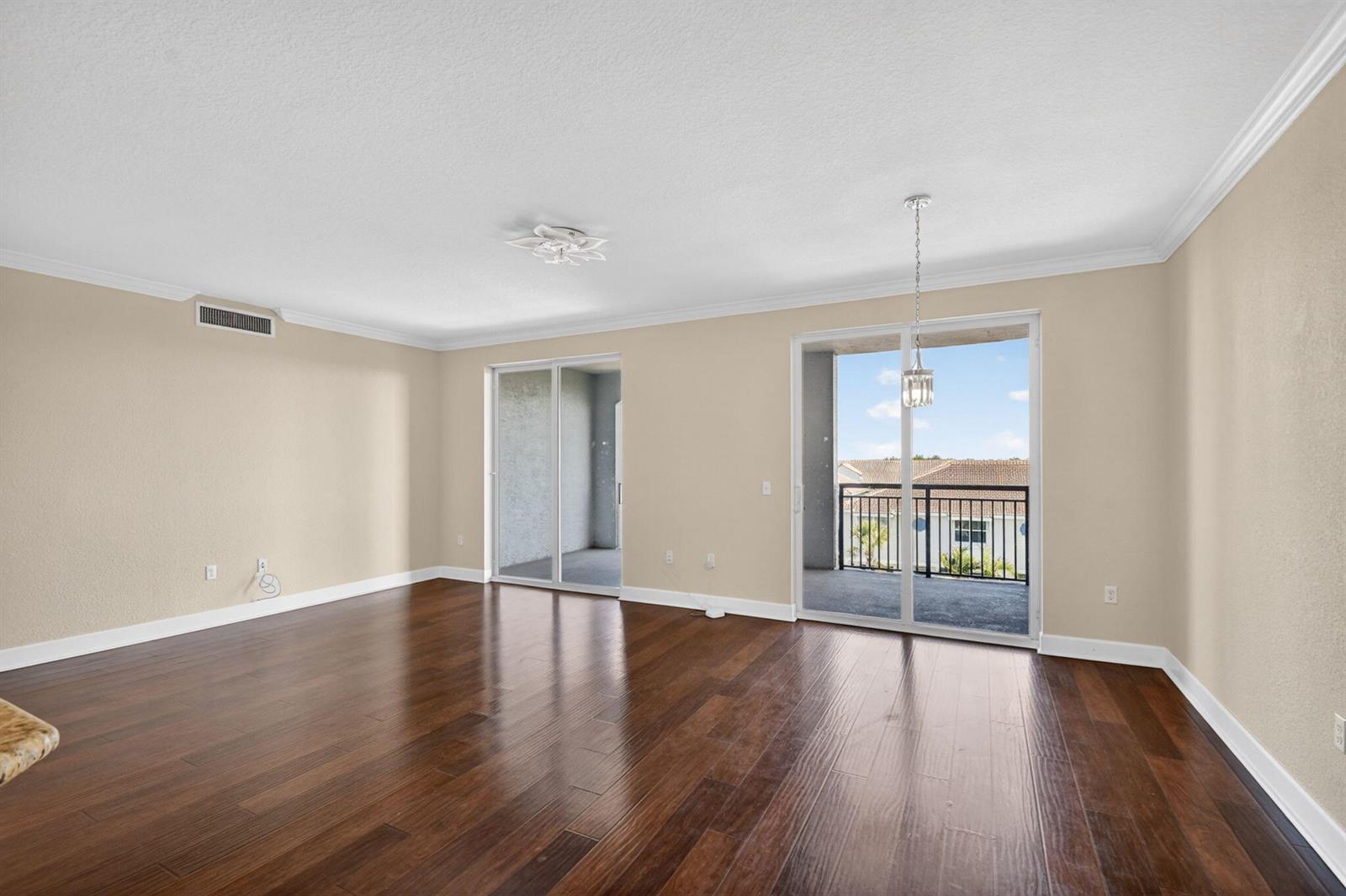 An empty living room with dark hardwood floors, beige walls, and two sliding glass doors — 1660 Renaissance Commons Boulevard # 2517, Boynton Beach FL 33426, BOYNTON BEACH, FL