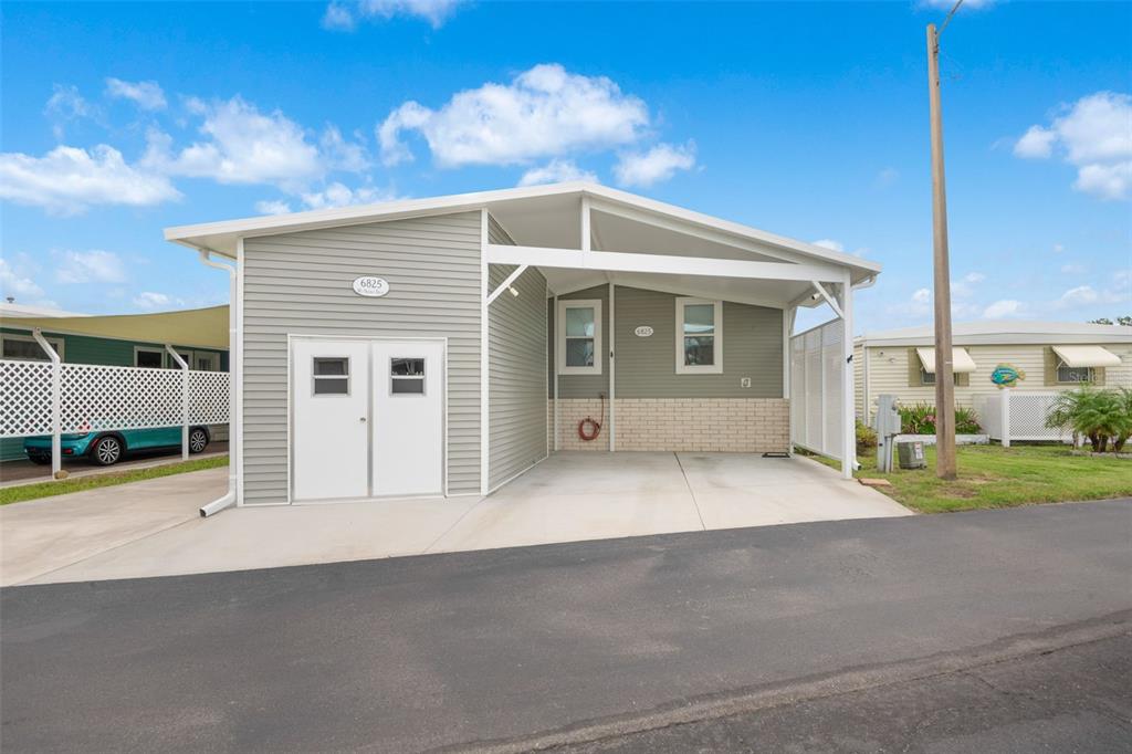 A single-story manufactured home with grey siding, a white carport, and a double-door storage shed — 6825 MOUNT ORANGE DRIVE NE UNIT 390, ST PETERSBURG, FL