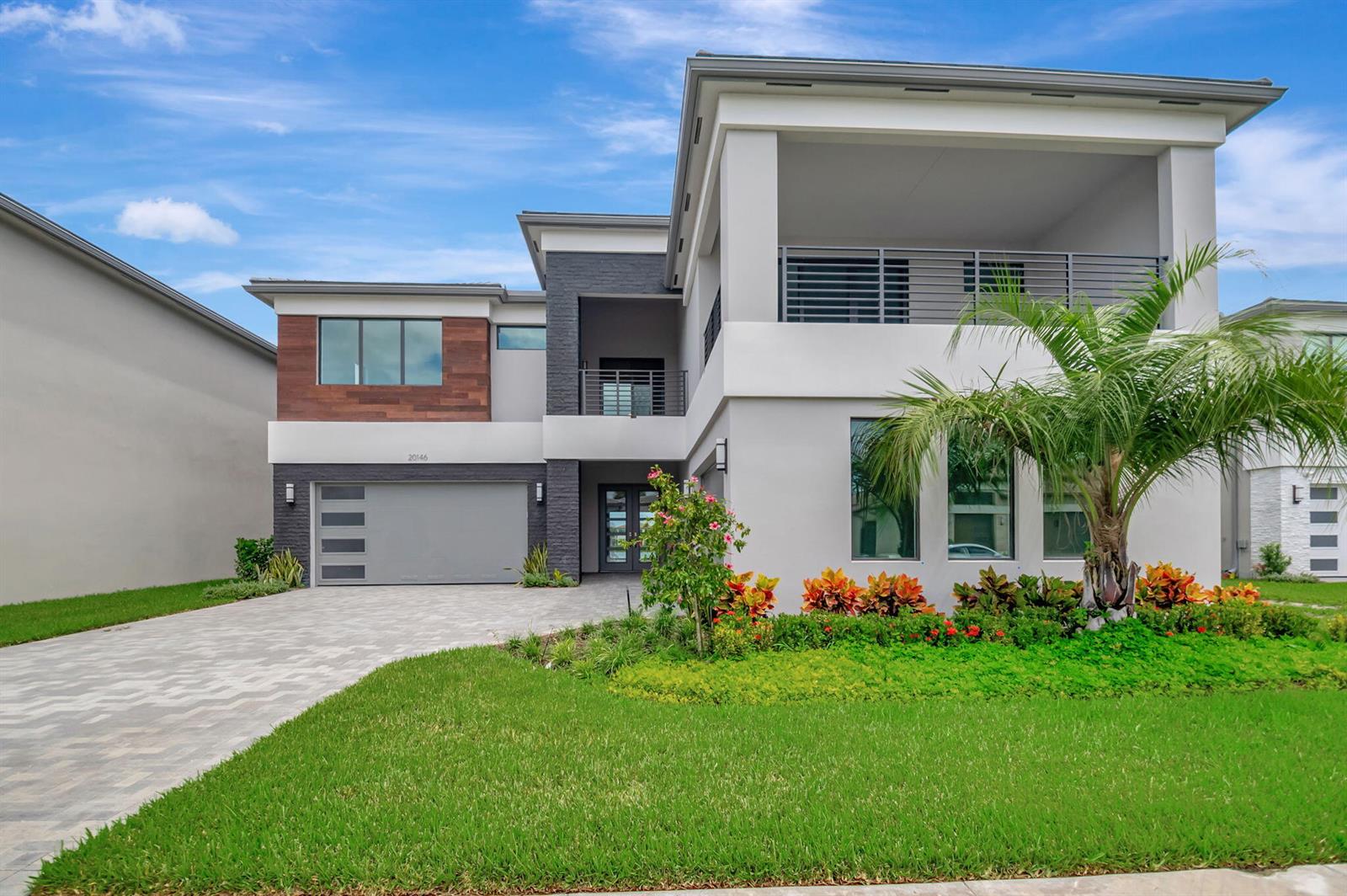 A modern two-story house features a gray garage, wood-paneled accents, and a large upper balcony — 20146 Casa De Campo Lane, Boca Raton FL 33434, BOCA RATON, FL