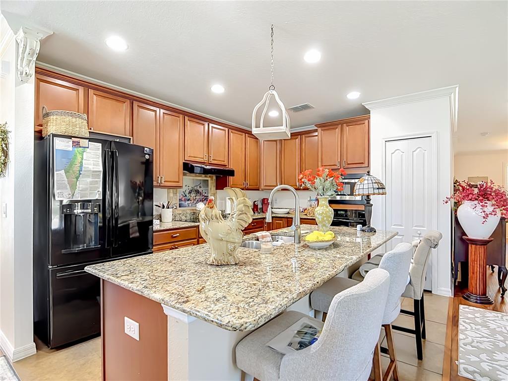 A kitchen features wood cabinets, granite countertops, a central island with seating, and black appliances — 5739 DORNICH DRIVE, AUBURNDALE, FL