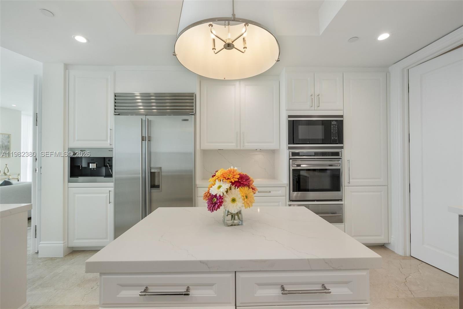 A white kitchen features a central island, stainless steel appliances, and a large pendant light — 10295 Collins Ave # 2203, Bal Harbour FL 33154, BAL HARBOUR, FL