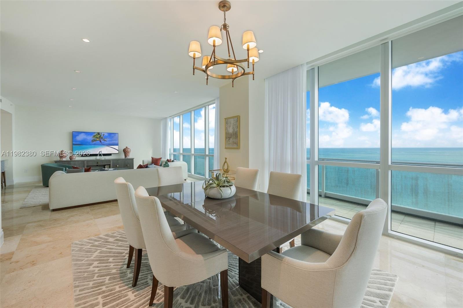 A dining area with a glossy table and chandelier overlooks the ocean through floor-to-ceiling windows — 10295 Collins Ave # 2203, Bal Harbour FL 33154, BAL HARBOUR, FL