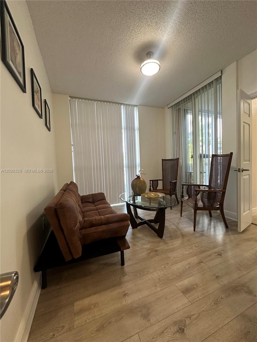 A living room features a brown sofa, two wooden chairs, a glass table, and flooring — 9755 NW 52nd St # 219, Doral FL 33178, DORAL, FL