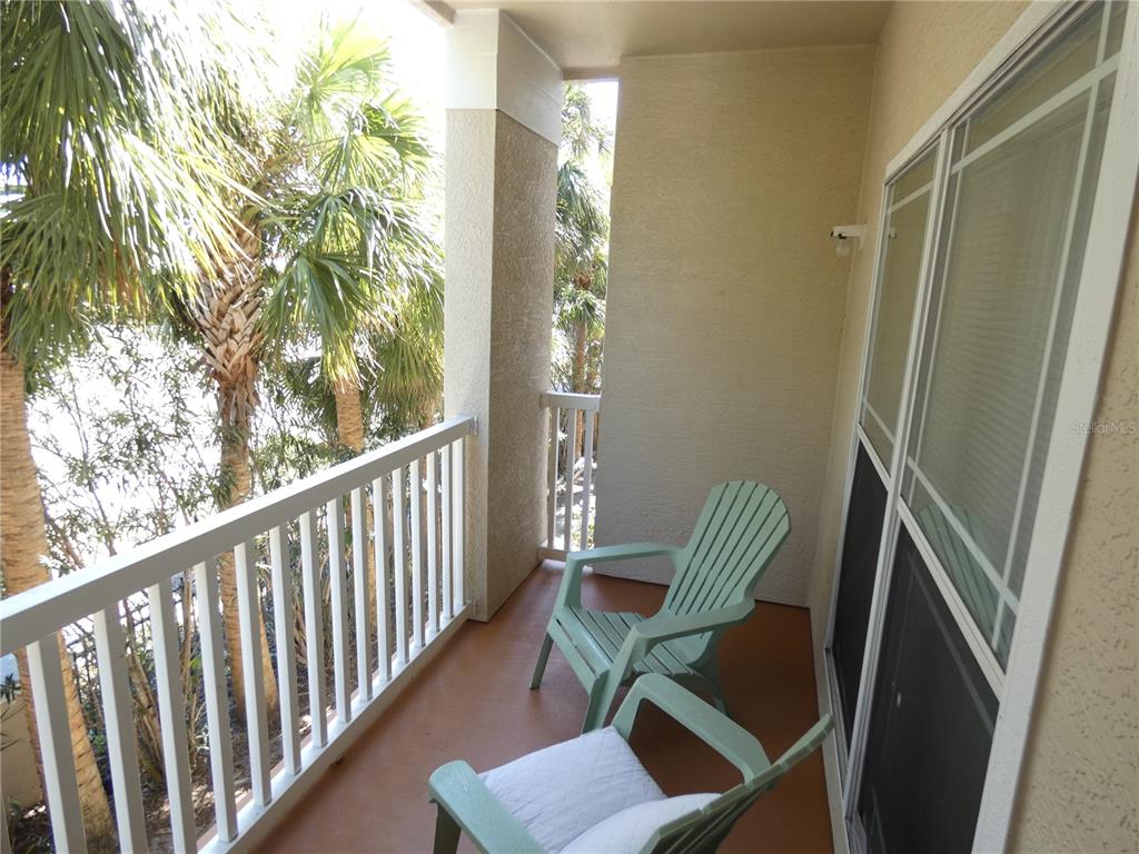 A balcony with two light green chairs overlooks palm trees and a body of water — 1216 S MISSOURI AVENUE UNIT 209, CLEARWATER, FL