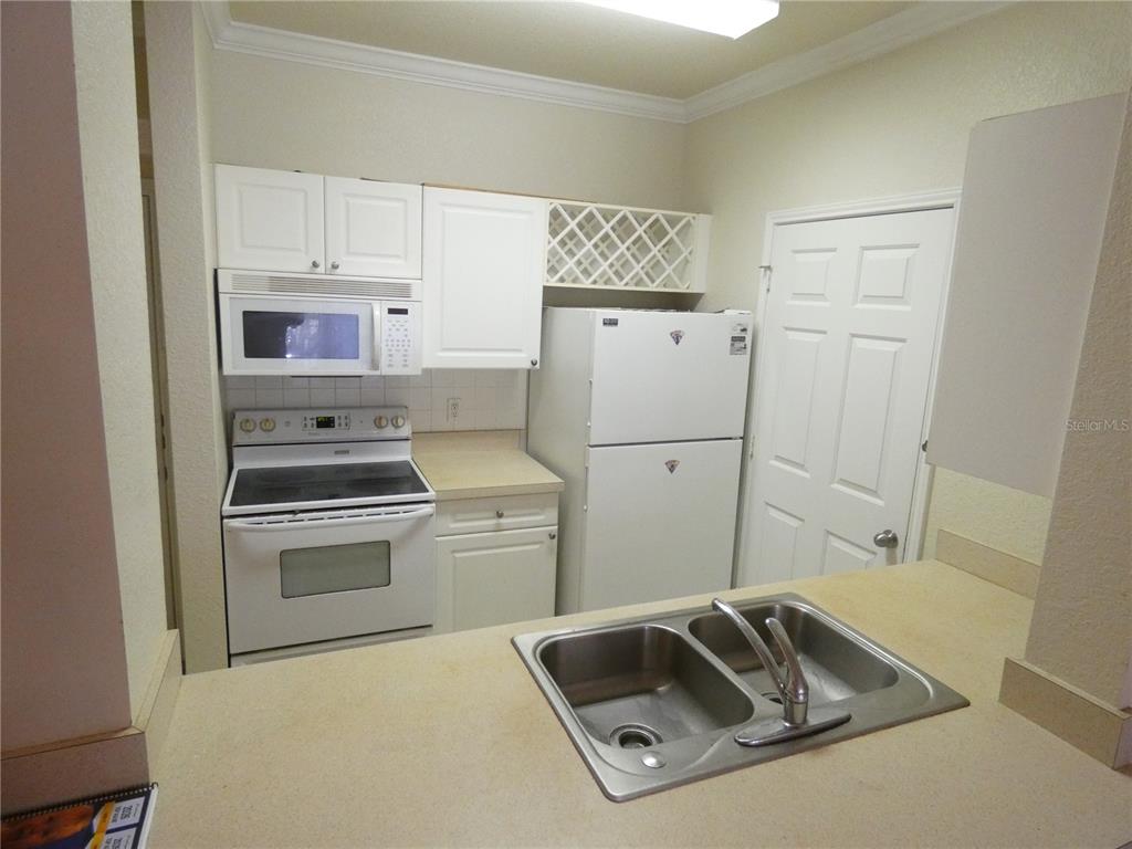 A kitchen features white cabinetry, white appliances, a double-basin sink, and a wine rack — 1216 S MISSOURI AVENUE UNIT 209, CLEARWATER, FL