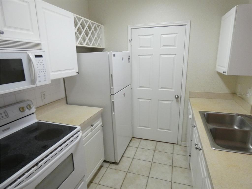 A kitchen features white cabinets, white appliances, a double sink, and light-colored tile flooring — 1216 S MISSOURI AVENUE UNIT 209, CLEARWATER, FL