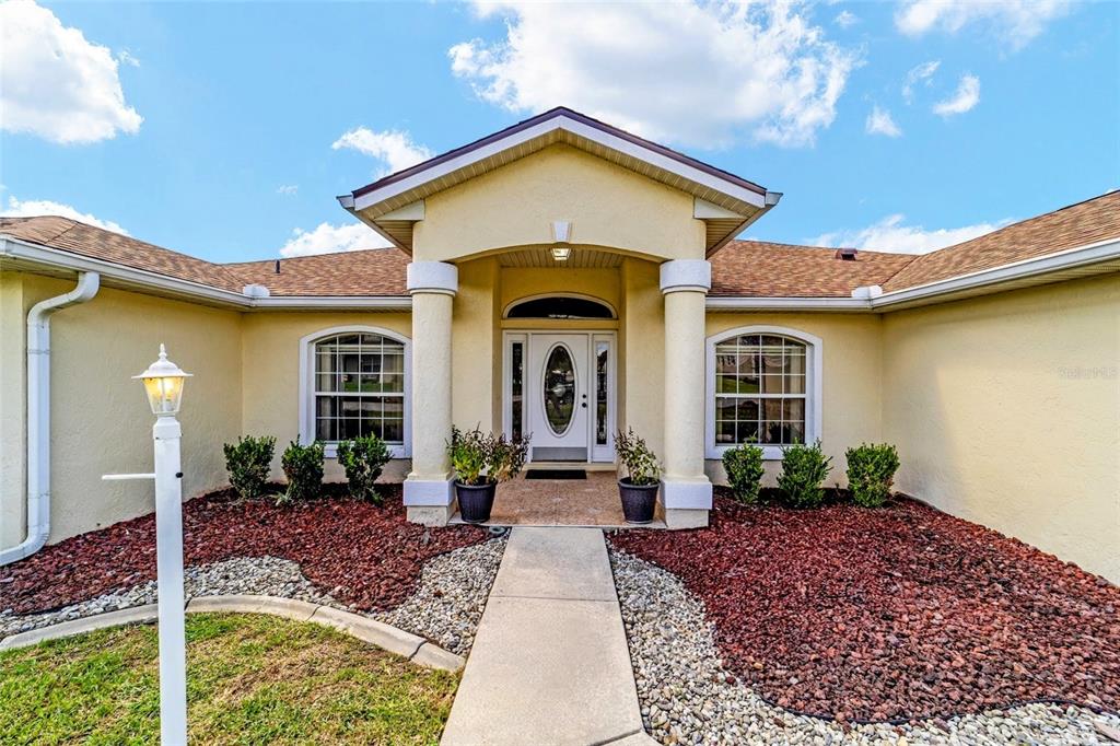 The exterior of a single-story house features a covered entryway with columns and red landscaping — 3465 SE 54TH AVENUE, OCALA, FL