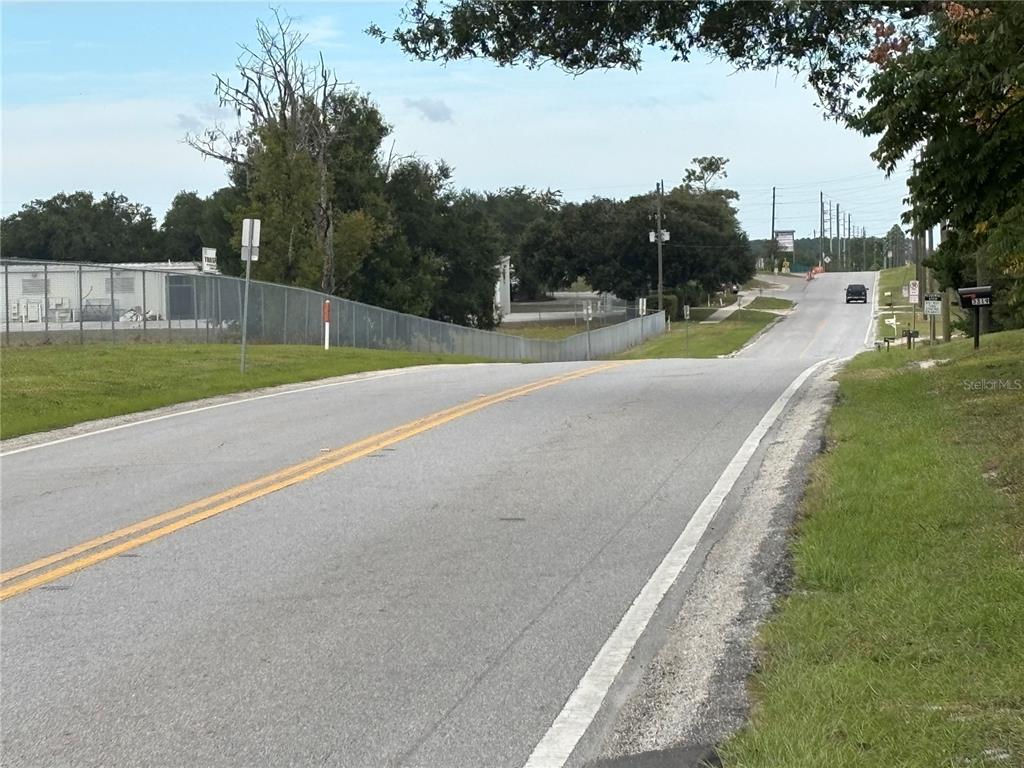 A two-lane asphalt road stretches into the distance past a fenced industrial property — 3427 GOLDEN GEM ROAD, APOPKA, FL