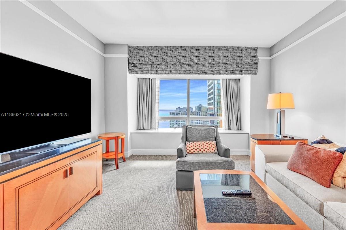 A living room features a large television, a gray armchair, and a window with ocean views — 1435 Brickell Ave # 3603, Miami FL 33131, MIAMI, FL