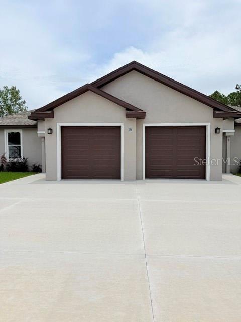A duplex building features two brown garage doors and a concrete driveway under a cloudy sky — 16 SLUMBERLAND PATH UNIT B, PALM COAST, FL