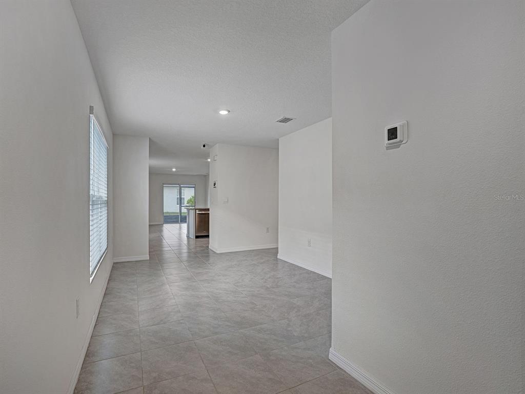 An interior view shows a tiled living area leading to a kitchen with sliding glass doors — 5586 LOGAN CAVE AVENUE, WIMAUMA, FL