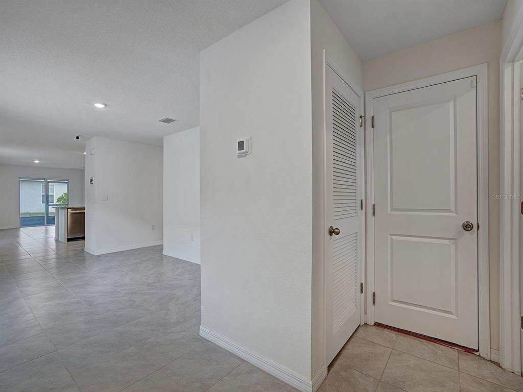 A hallway with tile flooring leads to an open living area with a kitchen — 5586 LOGAN CAVE AVENUE, WIMAUMA, FL