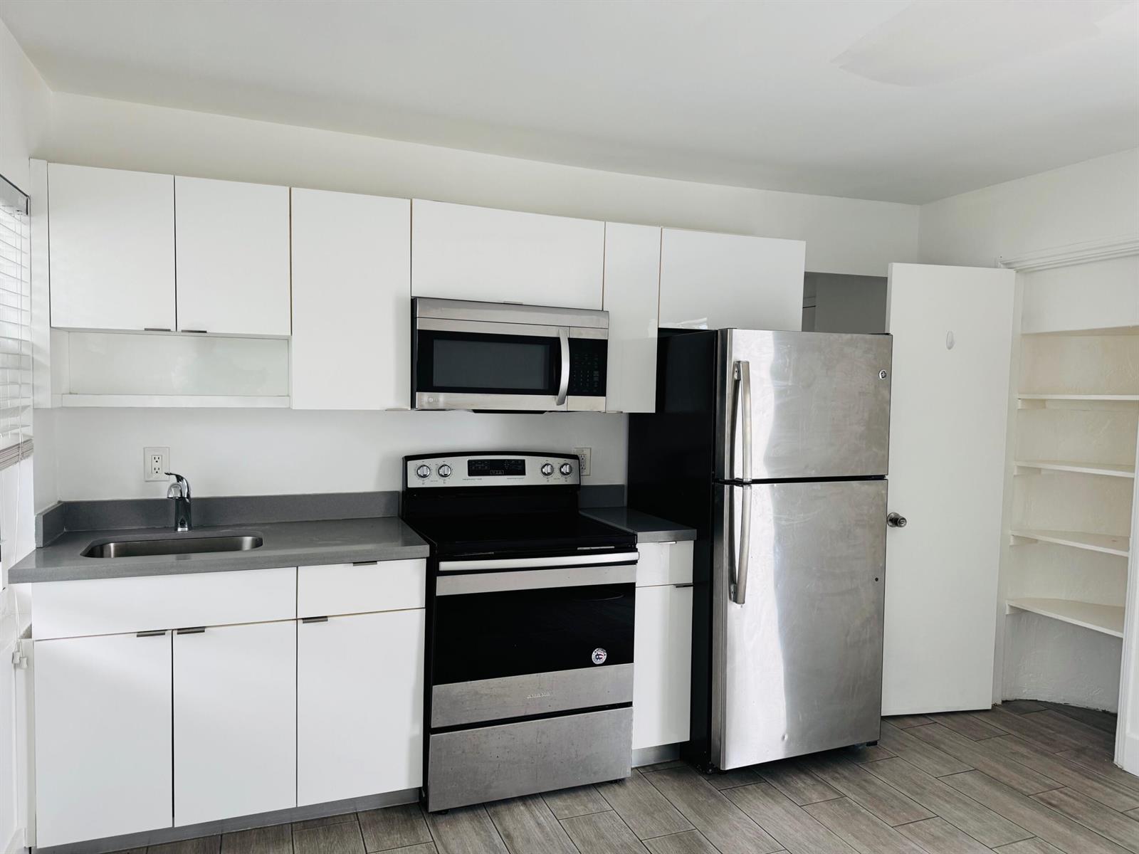 A kitchen features white cabinets, stainless steel appliances, a gray countertop, and wood-look flooring — 7910 Abbott Avenue # 6, Miami Beach FL 33141, MIAMI BEACH, FL
