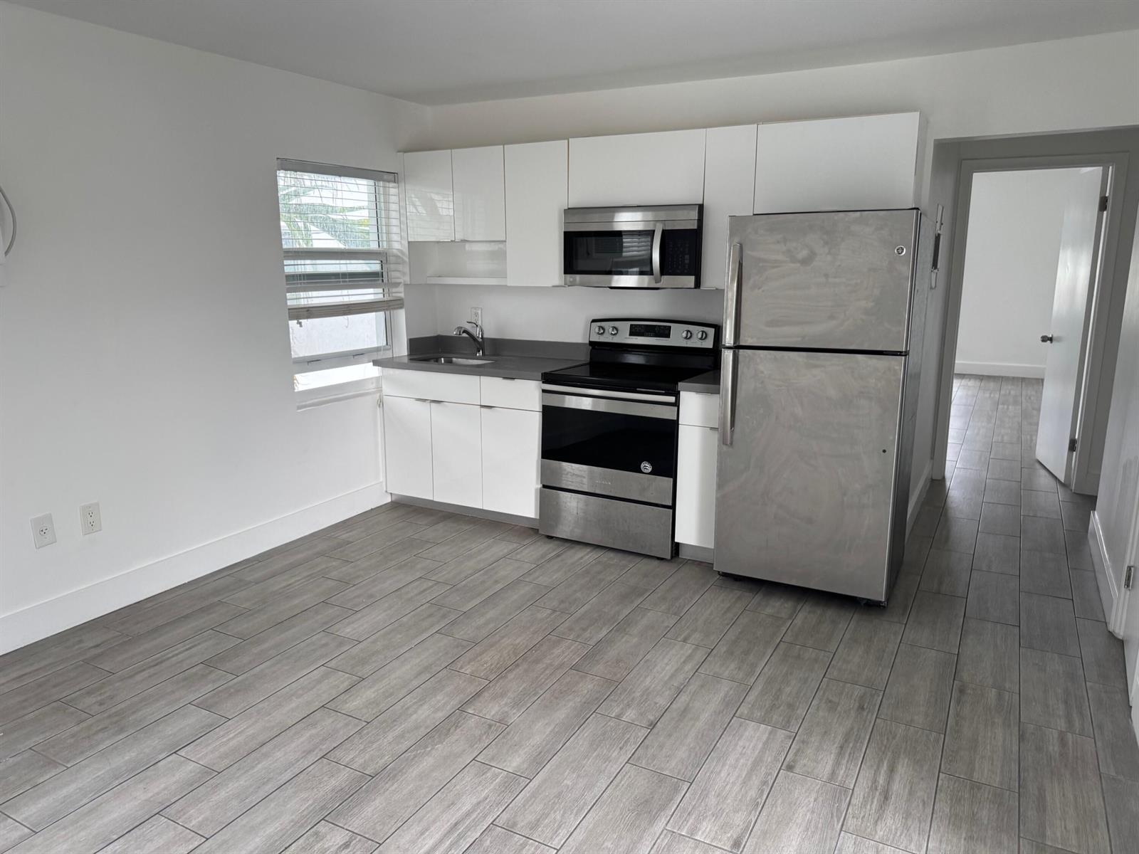 A kitchen features white cabinets, stainless steel appliances, and gray wood-look tile flooring — 7910 Abbott Avenue # 6, Miami Beach FL 33141, MIAMI BEACH, FL
