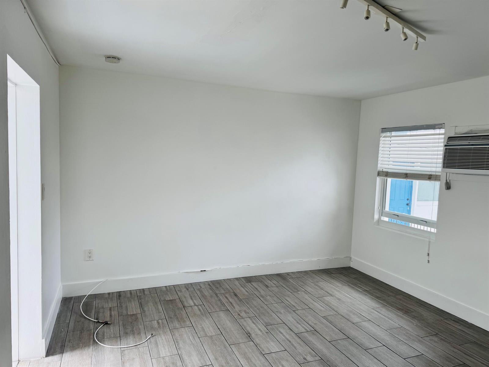 An empty room with white walls, wood-look tile flooring, a window air conditioner, and track lighting — 7910 Abbott Avenue # 6, Miami Beach FL 33141, MIAMI BEACH, FL