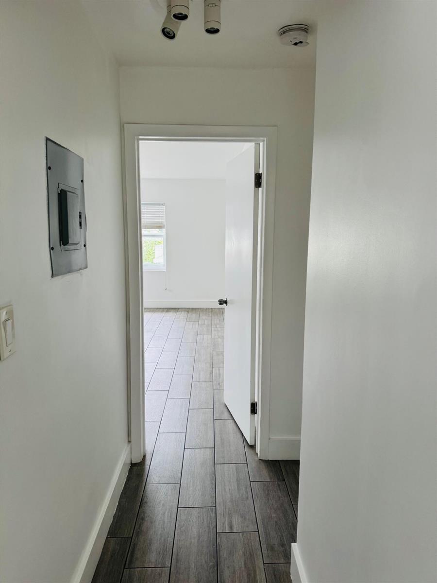 A hallway with wood-look tile flooring leads into a bedroom through an open doorway — 7910 Abbott Avenue # 6, Miami Beach FL 33141, MIAMI BEACH, FL