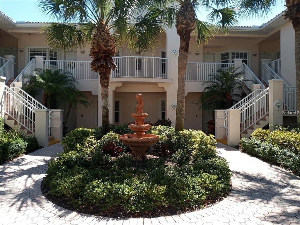 A two-story apartment building exterior features a central fountain surrounded by landscaping and staircases — 4216 CENTRAL SARASOTA PARKWAY UNIT 1325, SARASOTA, FL