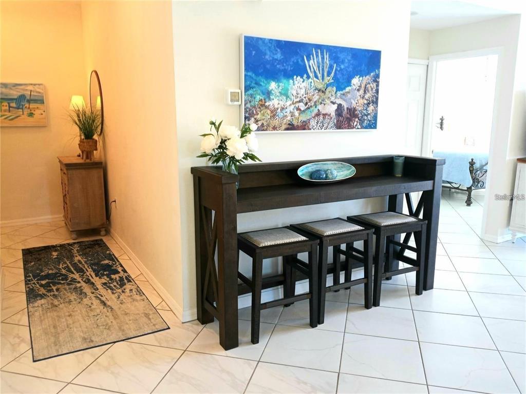 A dark wood console table with three matching stools sits in a tiled entryway — 4216 CENTRAL SARASOTA PARKWAY UNIT 1325, SARASOTA, FL