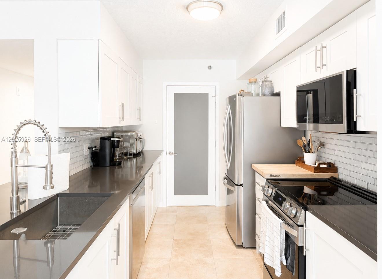 A galley kitchen features white cabinets, stainless steel appliances, and dark gray countertops — 3131 Clint Moore Rd # 107, Boca Raton FL 33496, BOCA RATON, FL