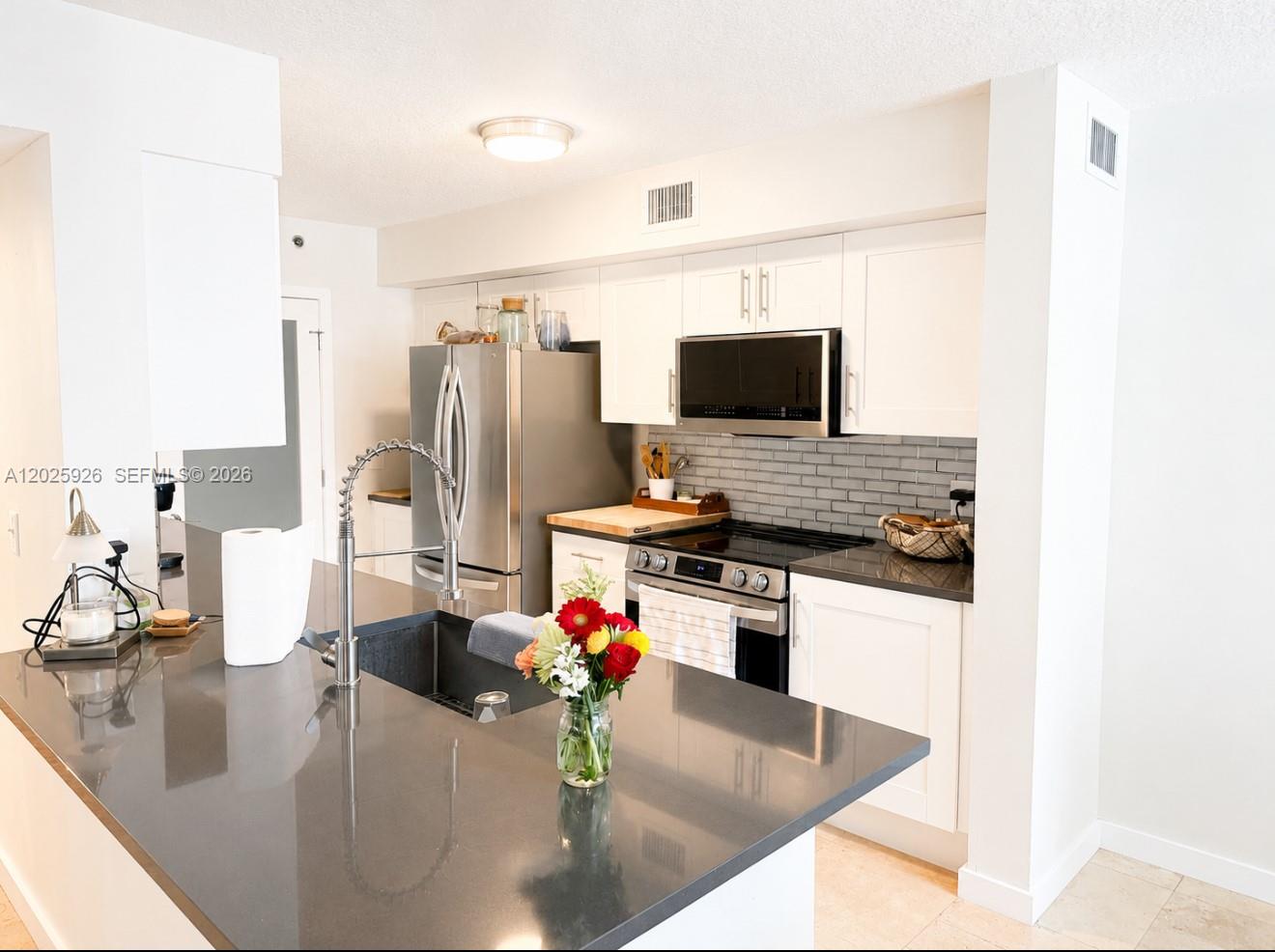 A kitchen features white cabinets, dark countertops, a stainless steel refrigerator, and a center island — 3131 Clint Moore Rd # 107, Boca Raton FL 33496, BOCA RATON, FL