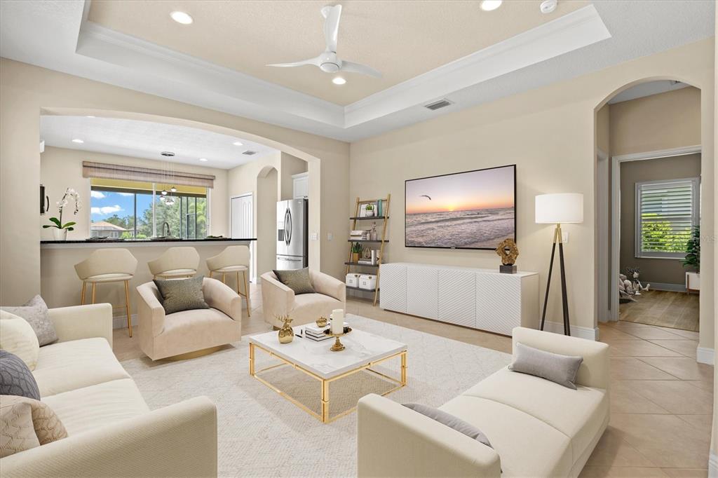 A bright living room features a tray ceiling, neutral furniture, a television, and a kitchen bar — 12717 DEEP BLUE PLACE, BRADENTON, FL