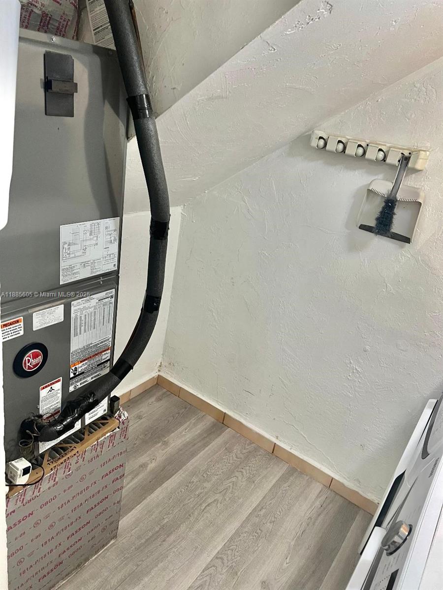 A utility closet contains a Rheem HVAC unit, wood-look flooring, and a wall-mounted dustpan — 1300 W 53rd St # 18, Hialeah FL 33012, HIALEAH, FL
