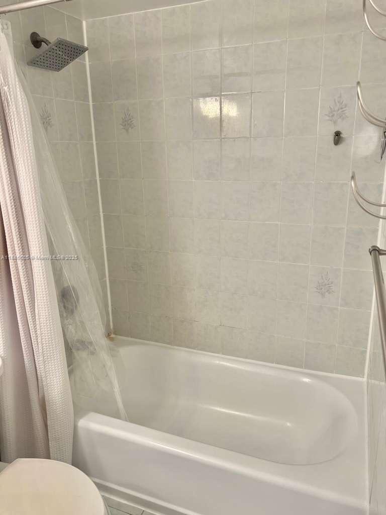 A white bathtub with a shower head is surrounded by light-colored square wall tiles — 1300 W 53rd St # 18, Hialeah FL 33012, HIALEAH, FL