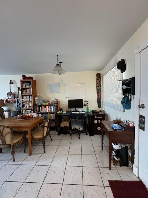 A room with tiled floors features a dining table, bookshelves, a desk, and a window — 2000 Biarritz Dr # 404, Miami Beach FL 33141, MIAMI BEACH, FL