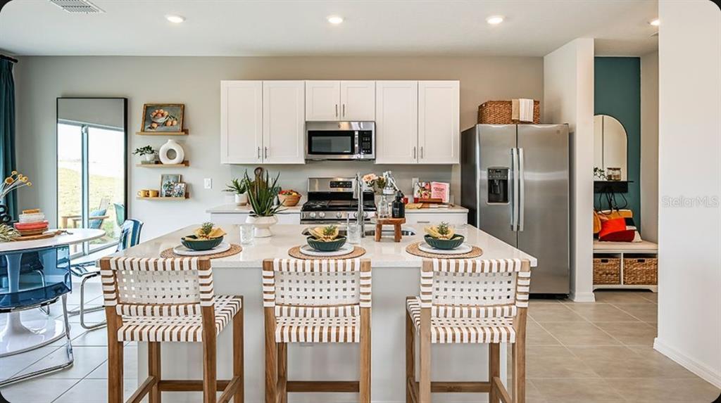 A modern kitchen features a central island with three woven stools and stainless steel appliances — 378 CORNERSTONE DRIVE, GROVELAND, FL