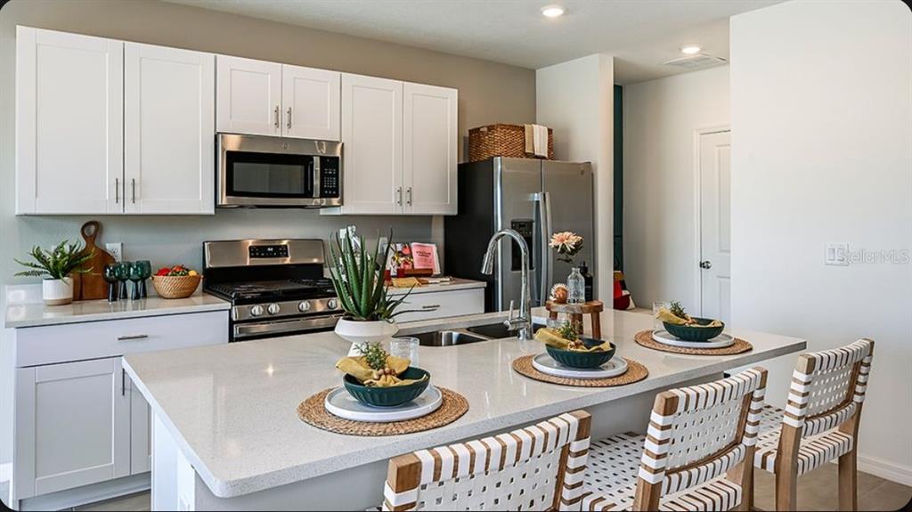 A kitchen features white cabinets, stainless steel appliances, a quartz island, and woven bar stools — 378 CORNERSTONE DRIVE, GROVELAND, FL