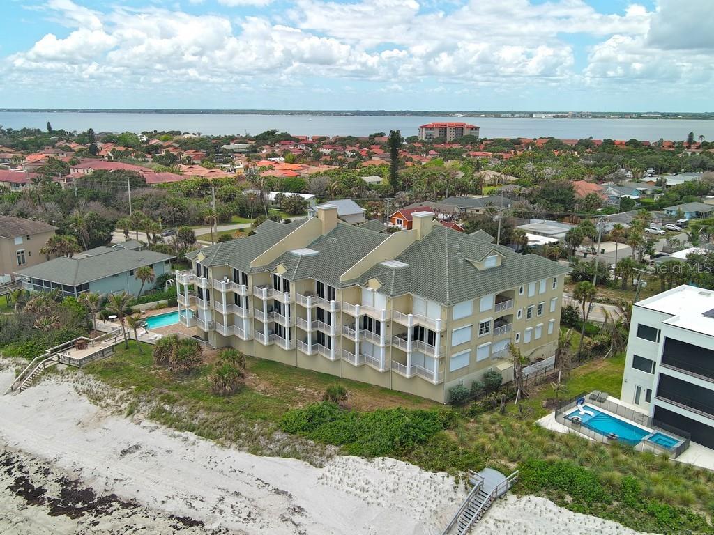 An aerial view shows a multi-story tan condominium building with balconies situated along a sandy beach — 3135 HIGHWAY A1A UNIT 202, MELBOURNE BEACH, FL