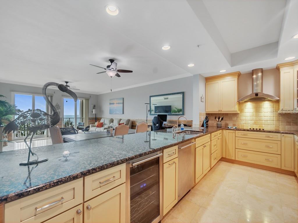 A kitchen with light wood cabinets and granite countertops overlooks an open-concept living area — 3135 HIGHWAY A1A UNIT 202, MELBOURNE BEACH, FL