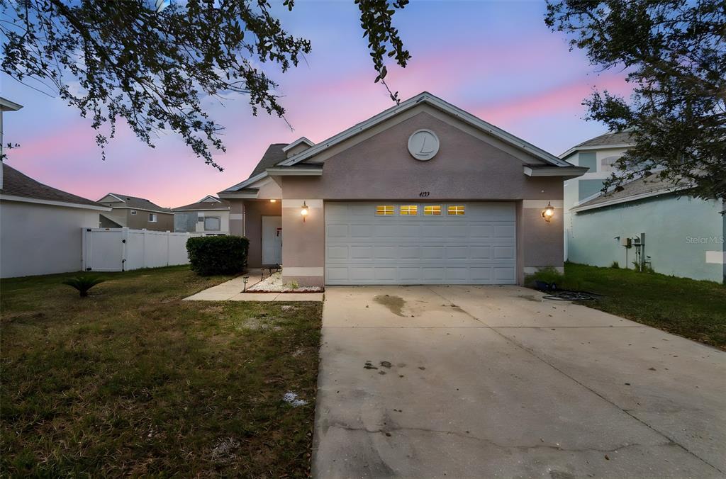 A single-story house with a two-car garage and a concrete driveway at sunset — 4135 ROCKY FORK TERRACE, ELLENTON, FL