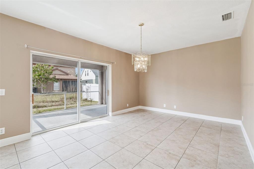 A dining room with beige walls, tile flooring, a crystal chandelier, and sliding glass doors — 4135 ROCKY FORK TERRACE, ELLENTON, FL