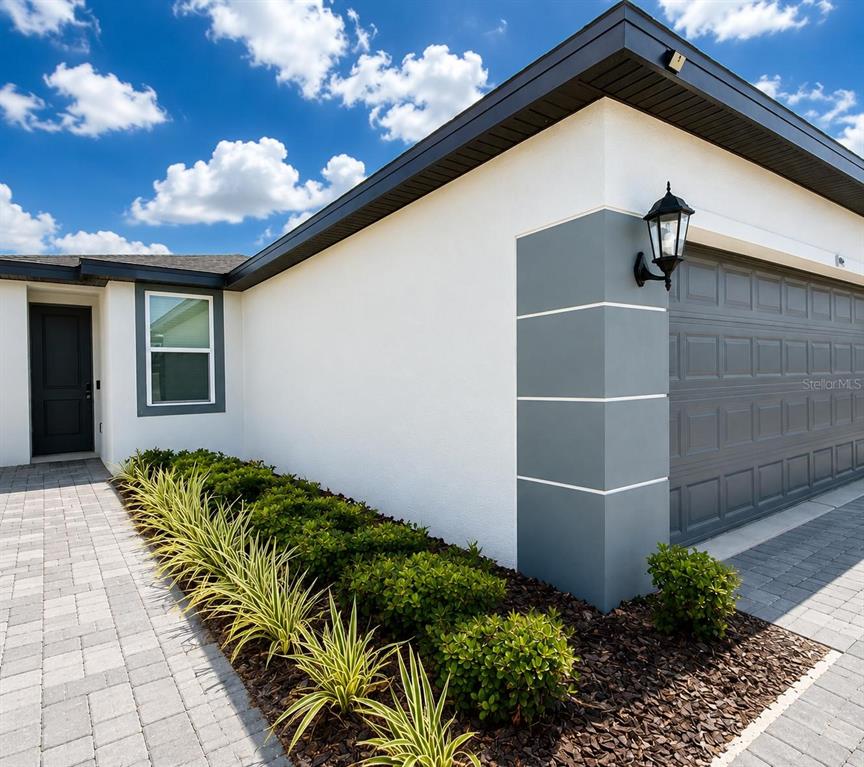 A modern house exterior features a gray garage door, white stucco walls, and landscaped garden beds — 5514 CLOVE ROW, HAINES CITY, FL