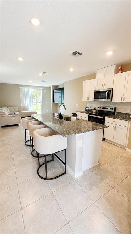 A kitchen with white cabinets and a granite island overlooks a living room area — 5514 CLOVE ROW, HAINES CITY, FL