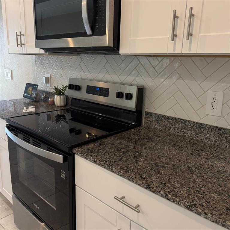 A kitchen features white cabinets, granite countertops, a stainless steel stove, and a herringbone backsplash — 5514 CLOVE ROW, HAINES CITY, FL