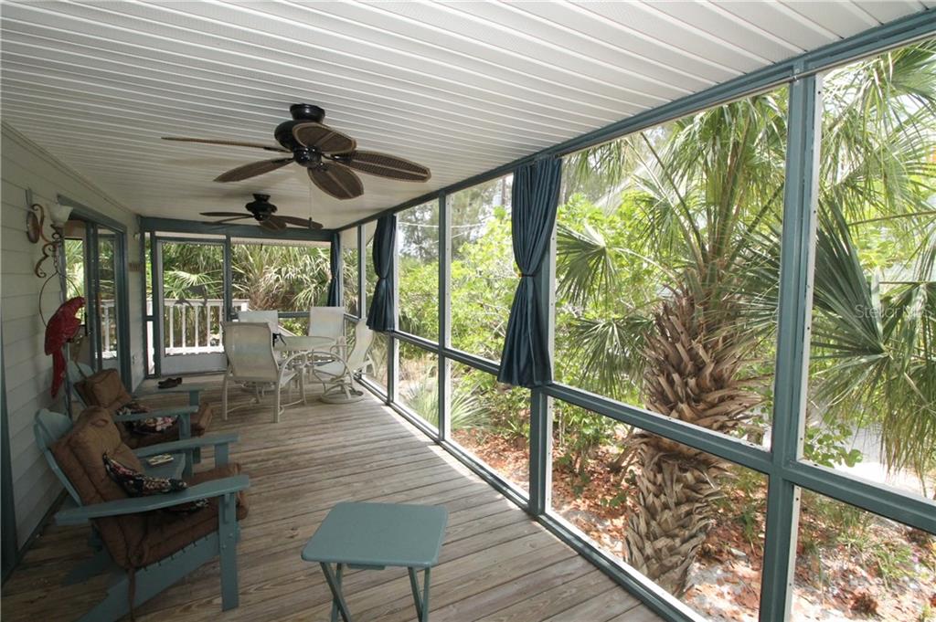 A screened-in porch with wooden decking, ceiling fans, outdoor furniture, and views of palm trees — 9352 LITTLE GASPARILLA ISLAND, PLACIDA, FL