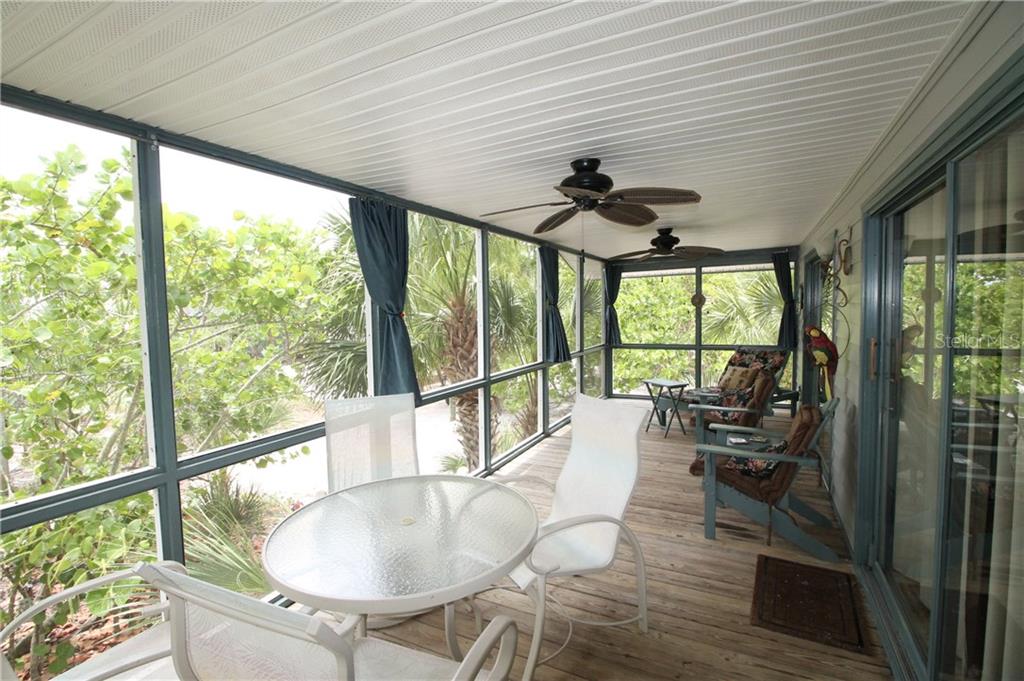 A screened-in porch with a wooden deck, patio furniture, and views of lush green trees — 9352 LITTLE GASPARILLA ISLAND, PLACIDA, FL