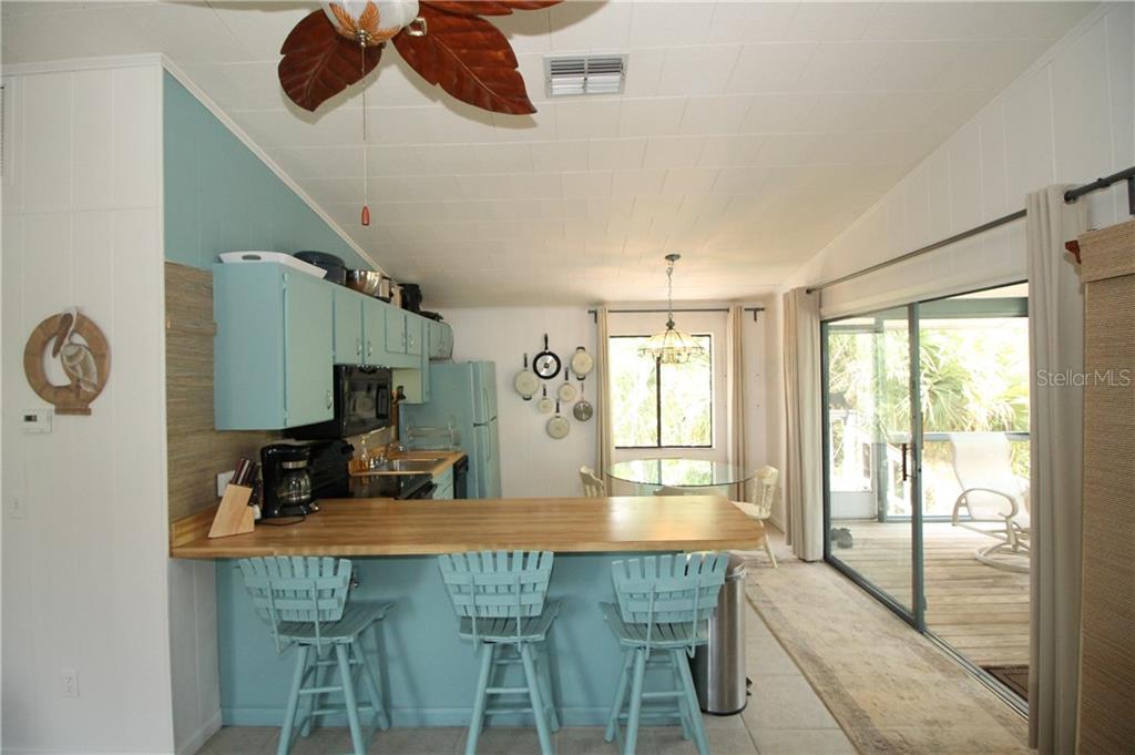 A kitchen features light blue cabinets, a wooden breakfast bar, and a sliding glass door — 9352 LITTLE GASPARILLA ISLAND, PLACIDA, FL