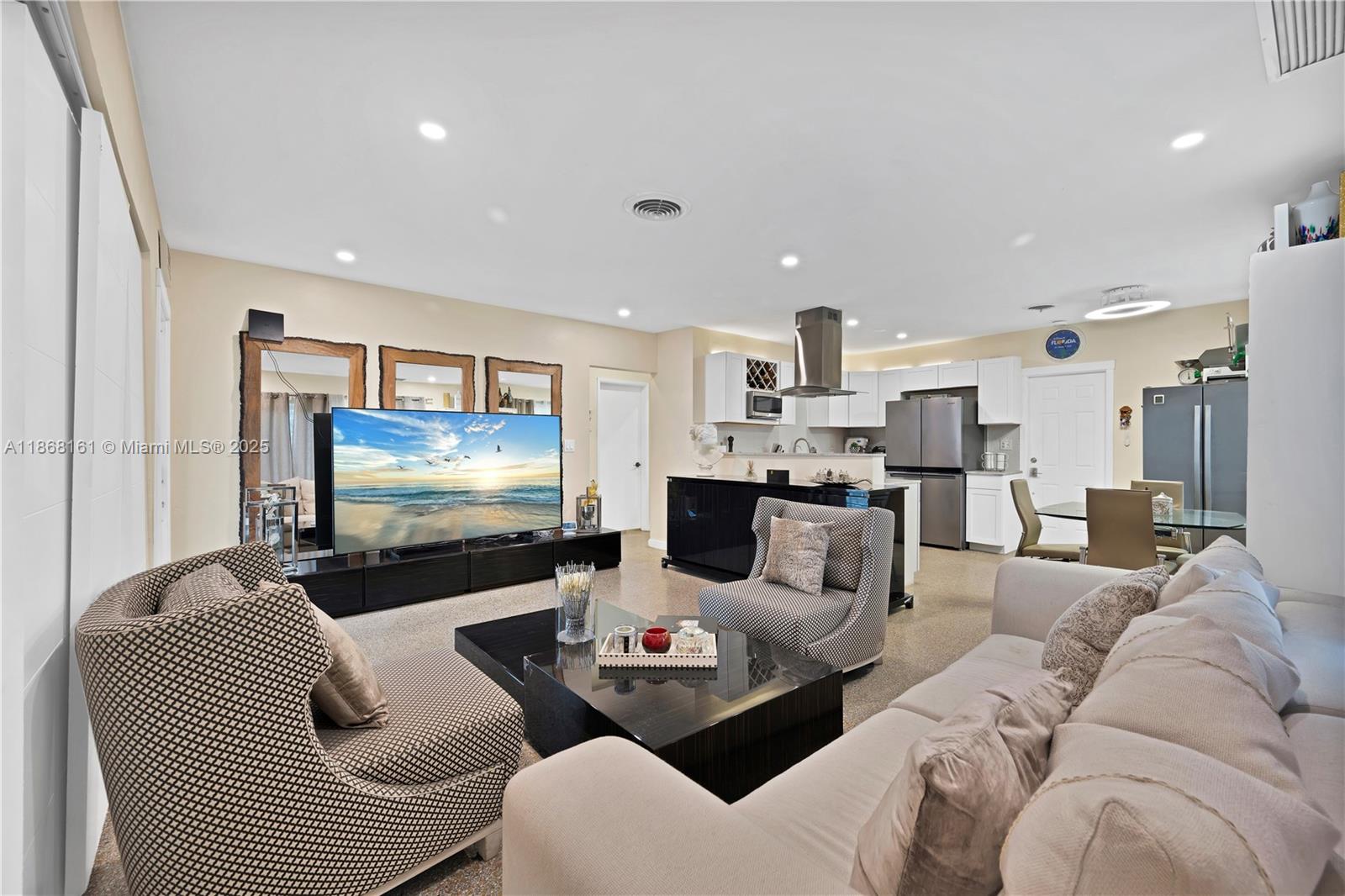 This open-concept living room features a television, a kitchen island, and neutral-toned furniture — 2615 Liberty St, Hollywood FL 33020, HOLLYWOOD, FL