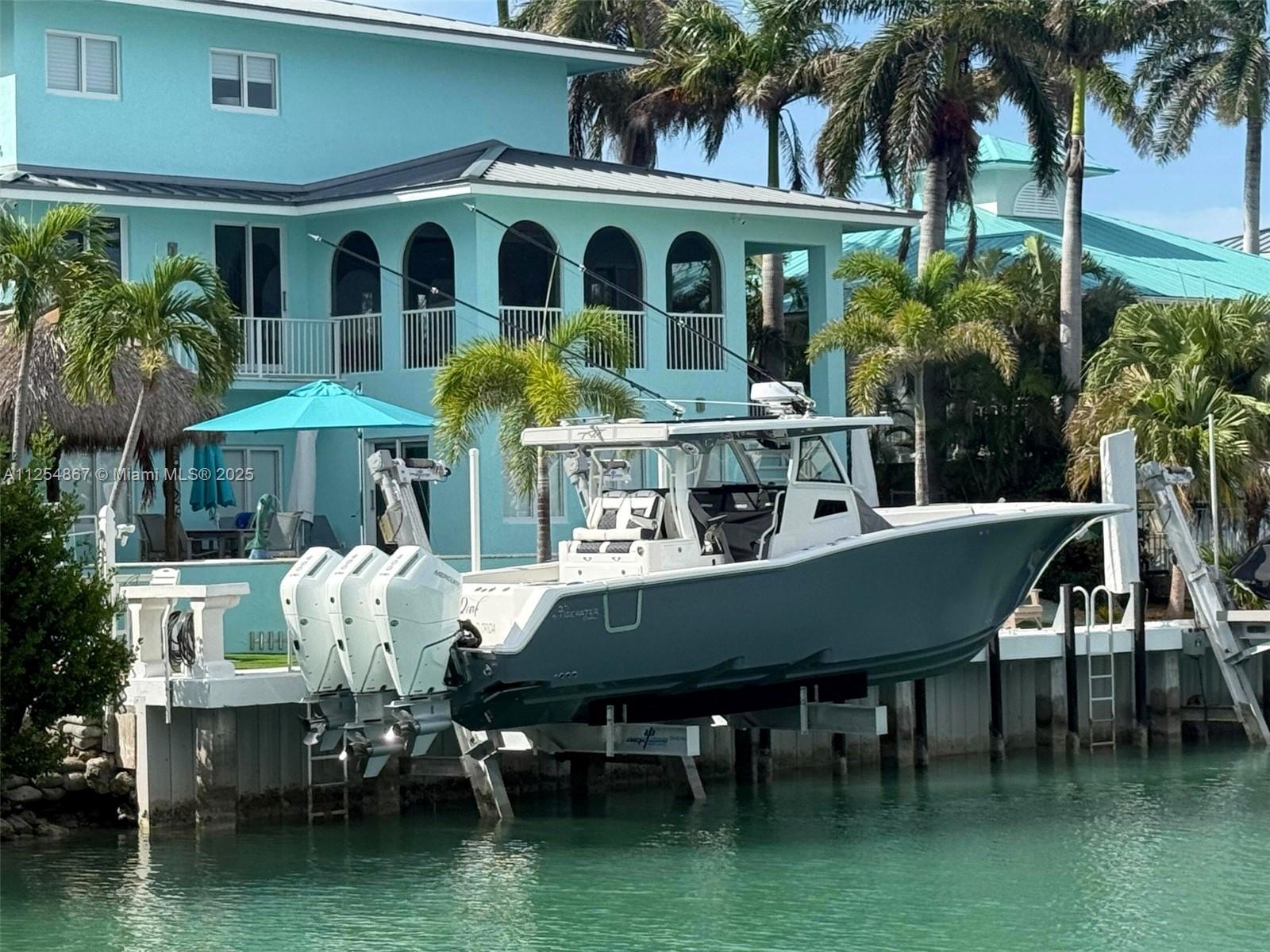 A large boat with three outboard motors is lifted on a dock beside a teal house — 124 S Indies, Marathon FL 33050, MARATHON, FL