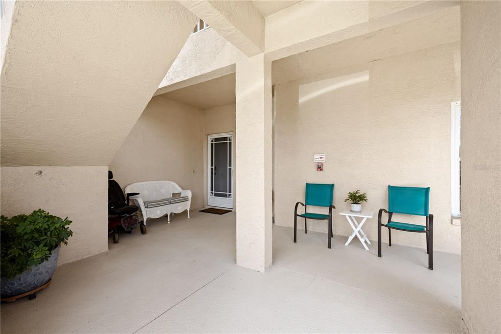 A covered patio features a white bench, two teal chairs, a small table, and stairs — 5800 SABAL TRACE DRIVE UNIT 301, NORTH PORT, FL