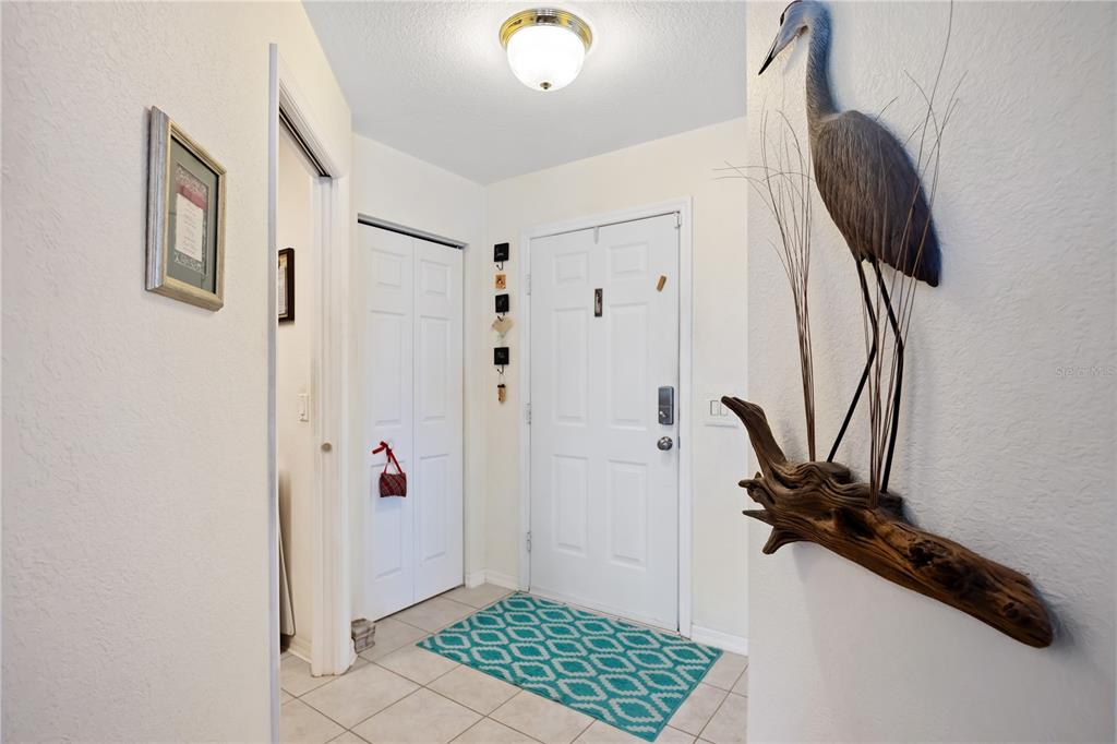 A tiled entryway features a white front door, a closet, and a decorative heron wall sculpture — 5800 SABAL TRACE DRIVE UNIT 301, NORTH PORT, FL